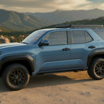 A blue Toyota 4Runner SUV parked on a dirt road with mountains in the background, shown from a three-quarter side angle.
